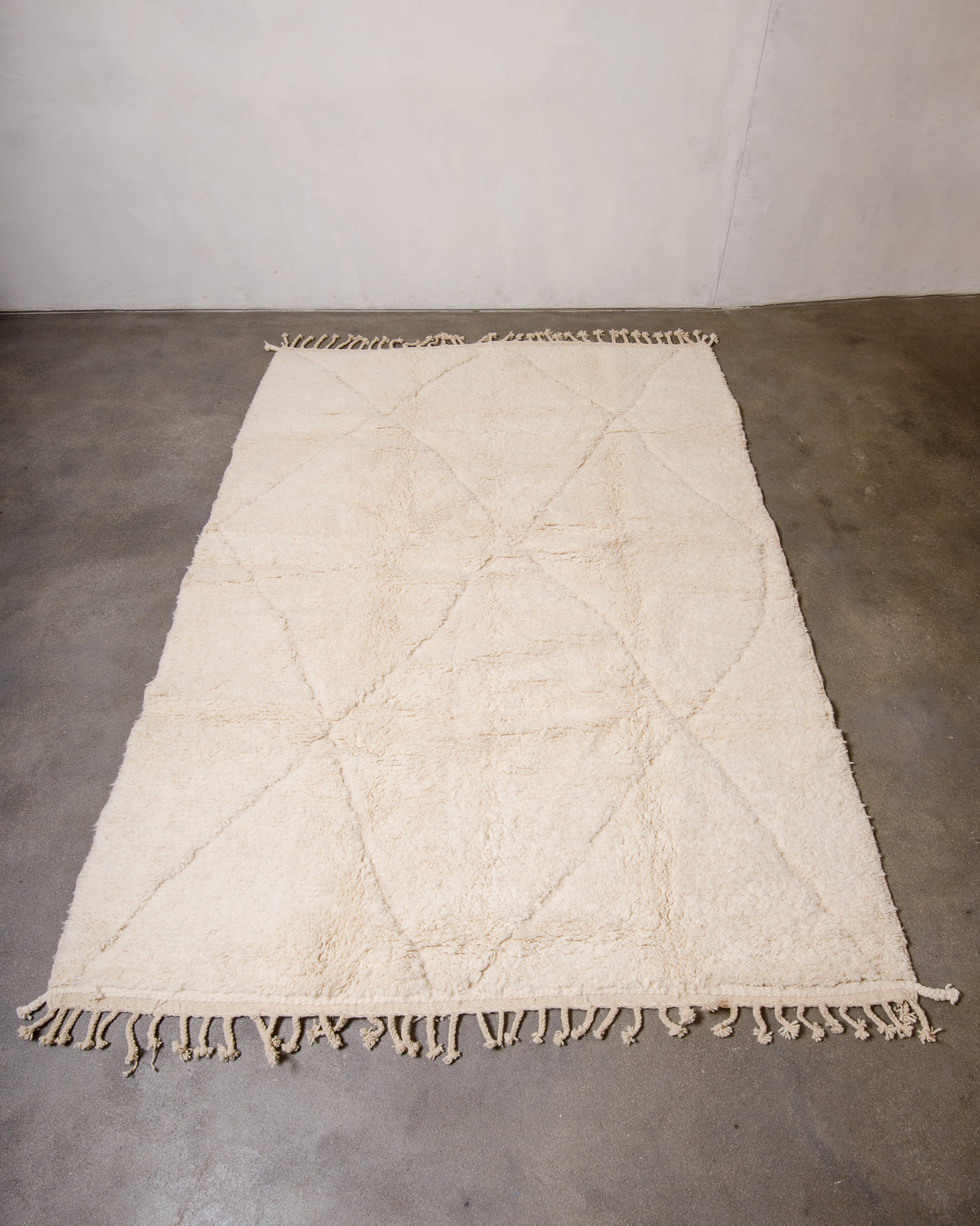 Wool Berberlin Beniourain rug in natural cream with a subtle diamond design, laying on concrete floor.